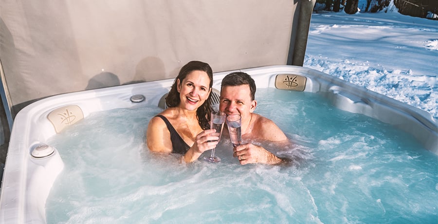 A heartwarming scene with a couple huddled in a steaming Serenity hot tub. Snow is visible in the surrounding garden, but the family is warm and cosy. 