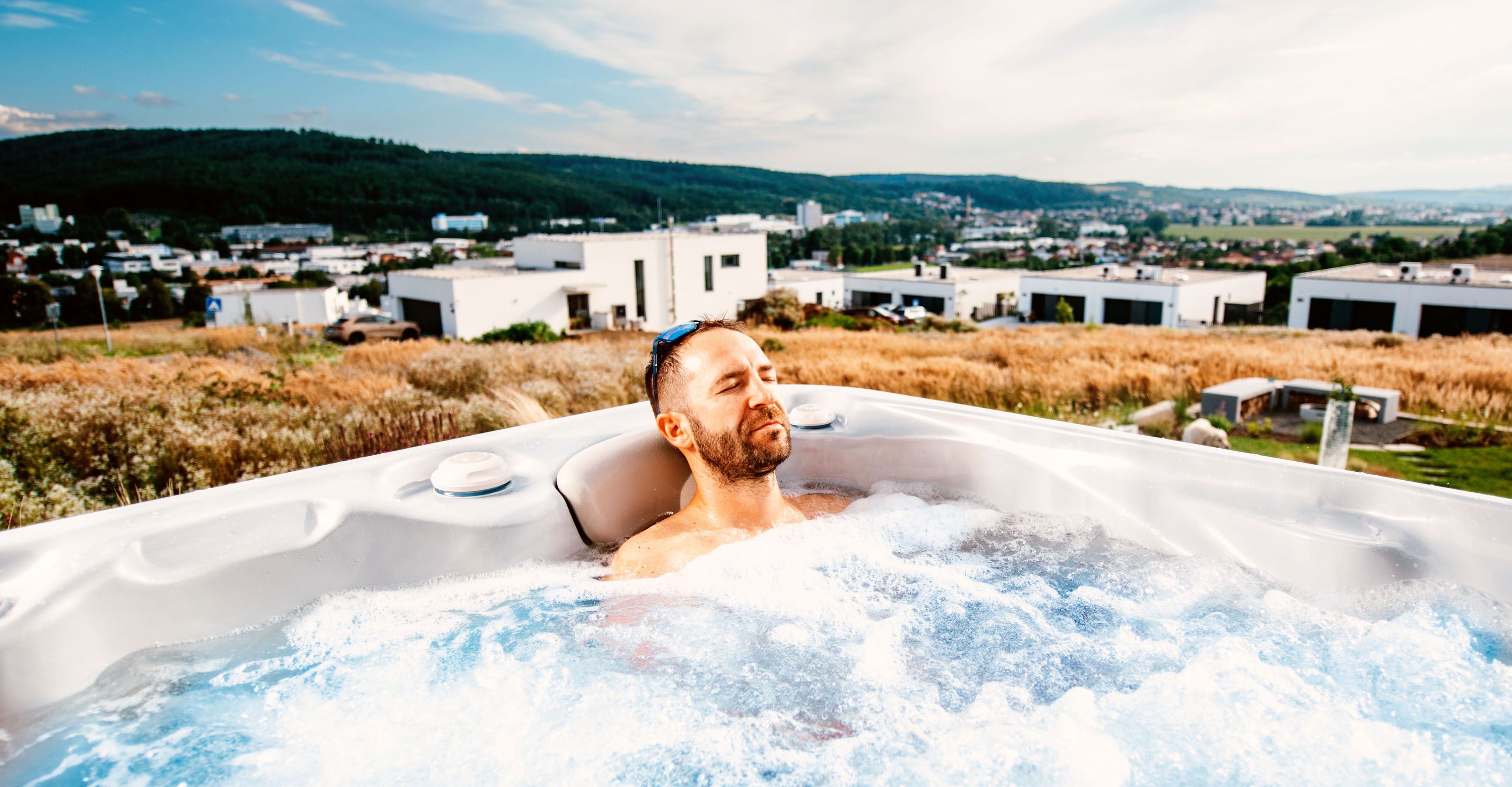 A middle-aged man closing his eyes in relaxation while leaning against the ergonomic headrest of a Hydropool hot tub, demonstrating home-based hydrotherapy for neck and shoulder tension.