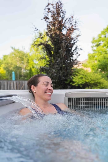 A woman smiles while relaxing under the waterfall jet of her constant current swim spa.