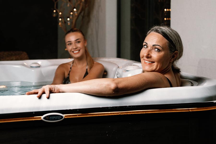 A mother and daughter relaxing together in an energy-efficient Hydropool hot tub, demonstrating how the Triple Thermal Shield insulation keeps the water warm for year-round family use in the North West climate.