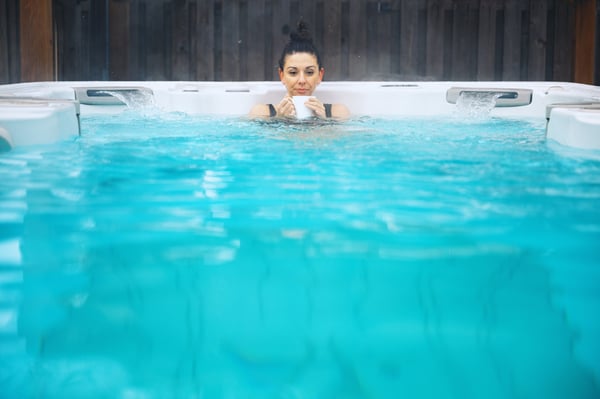 A woman calmly enjoying her morning coffee on a crisp Winter day, she's chest deep in her hot swim spa.