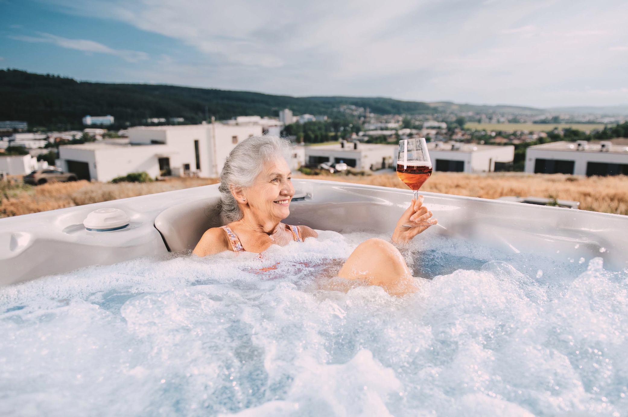 A senior woman enjoys a hot tub with drink in her hand. 